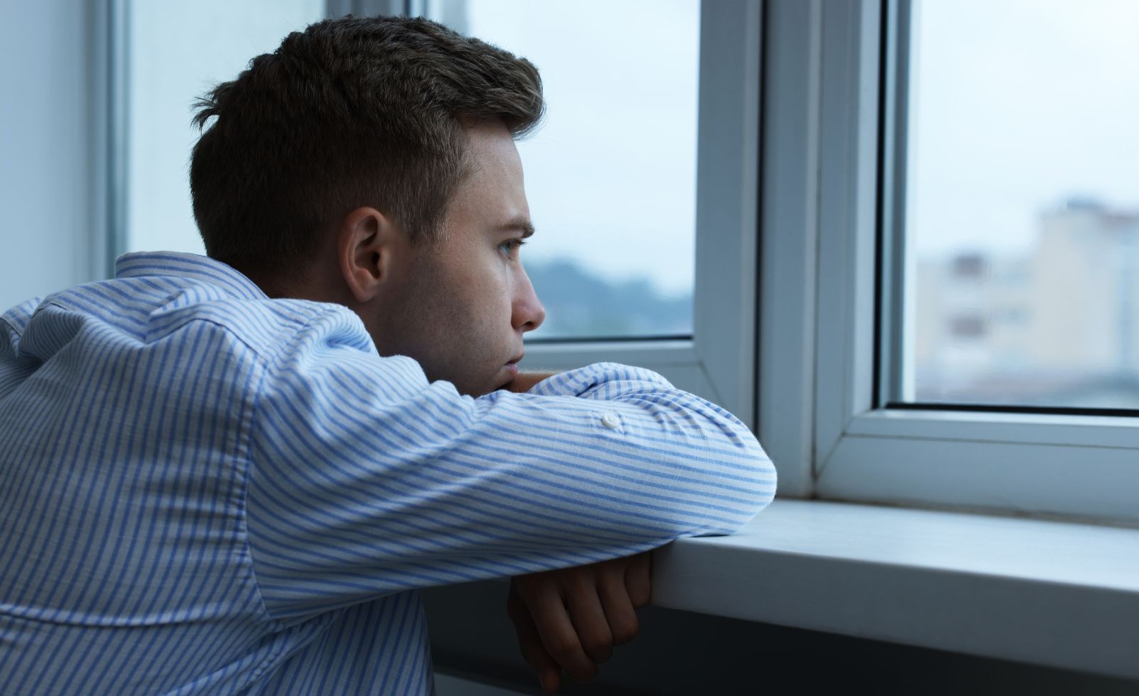 chłopak oparty o parapet patrzy przez okno
